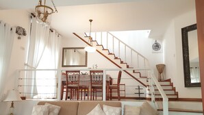 Ein Wohnzimmer mit Sofa, Esstisch, Stühlen, einer Treppe und einer Chandelüster.