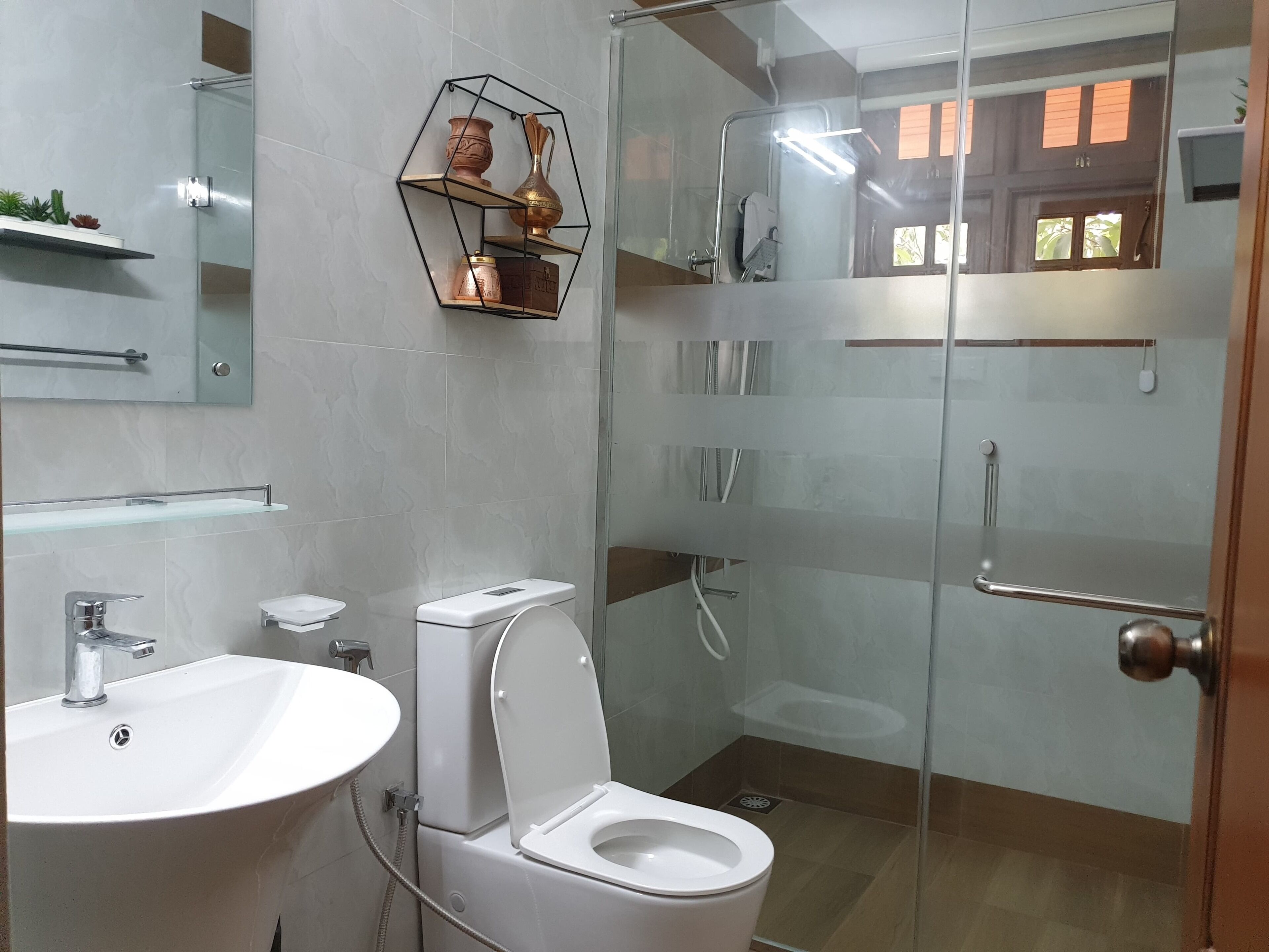 Casa de banho moderna com chuveiro envidraçado, sanita branca e uma grande pia.