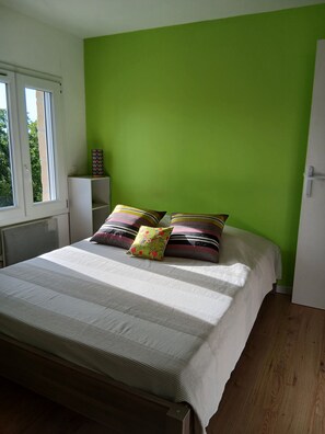 A bedroom with a bed, pillows, a window, and a white wardrobe.