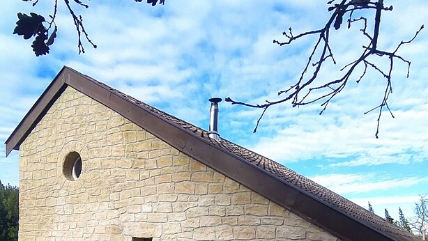 Ein Steinhaus mit geneigtem Dach, einem Schornstein und einer kleinen Veranda mit einer Bank und Topfpflanzen.