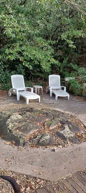 Two white lounge chairs with a small table in a garden area with a stone path and greenery in the background. - House 6/8 persons with swimming pool in a quiet area (La Capelle-et-Masmolène)