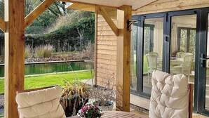 An outdoor wooden deck with a table and chairs, a garden view, and a glass door leading to an indoor area. - Private Garden House, Historic Castle Estate, Pool, Tennis & Gardens (Togher)