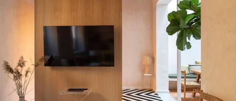 Sala de estar moderna com uma televisão de tela plana grande fixada numa parede revestida de madeira, uma pequena mesa lateral com abajur, uma planta grande em vaso e um tapete com padrão preto e branco.