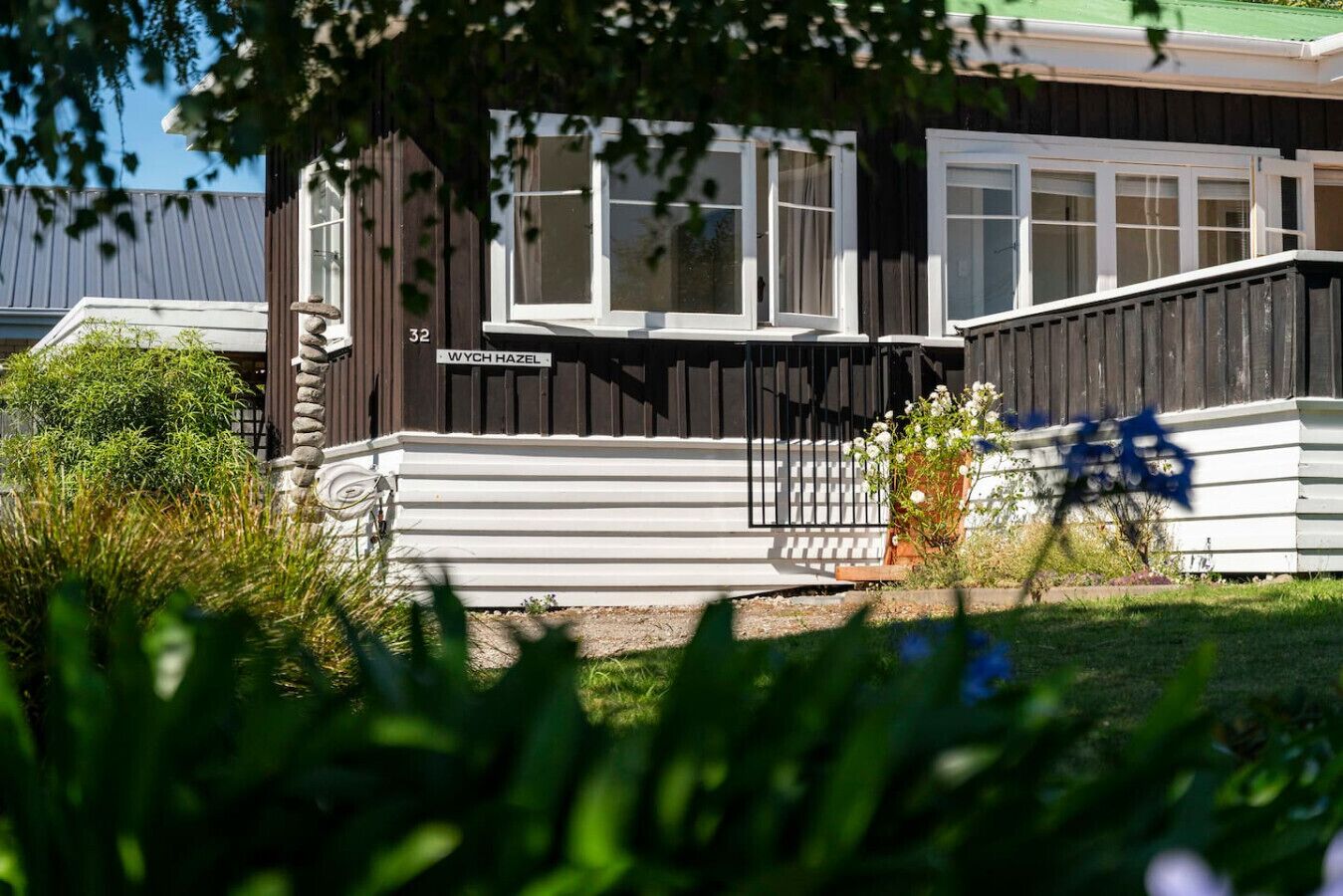 A modern house with a white exterior, a dark brown fence, and a sign that reads "WYCH HAZEL 32".