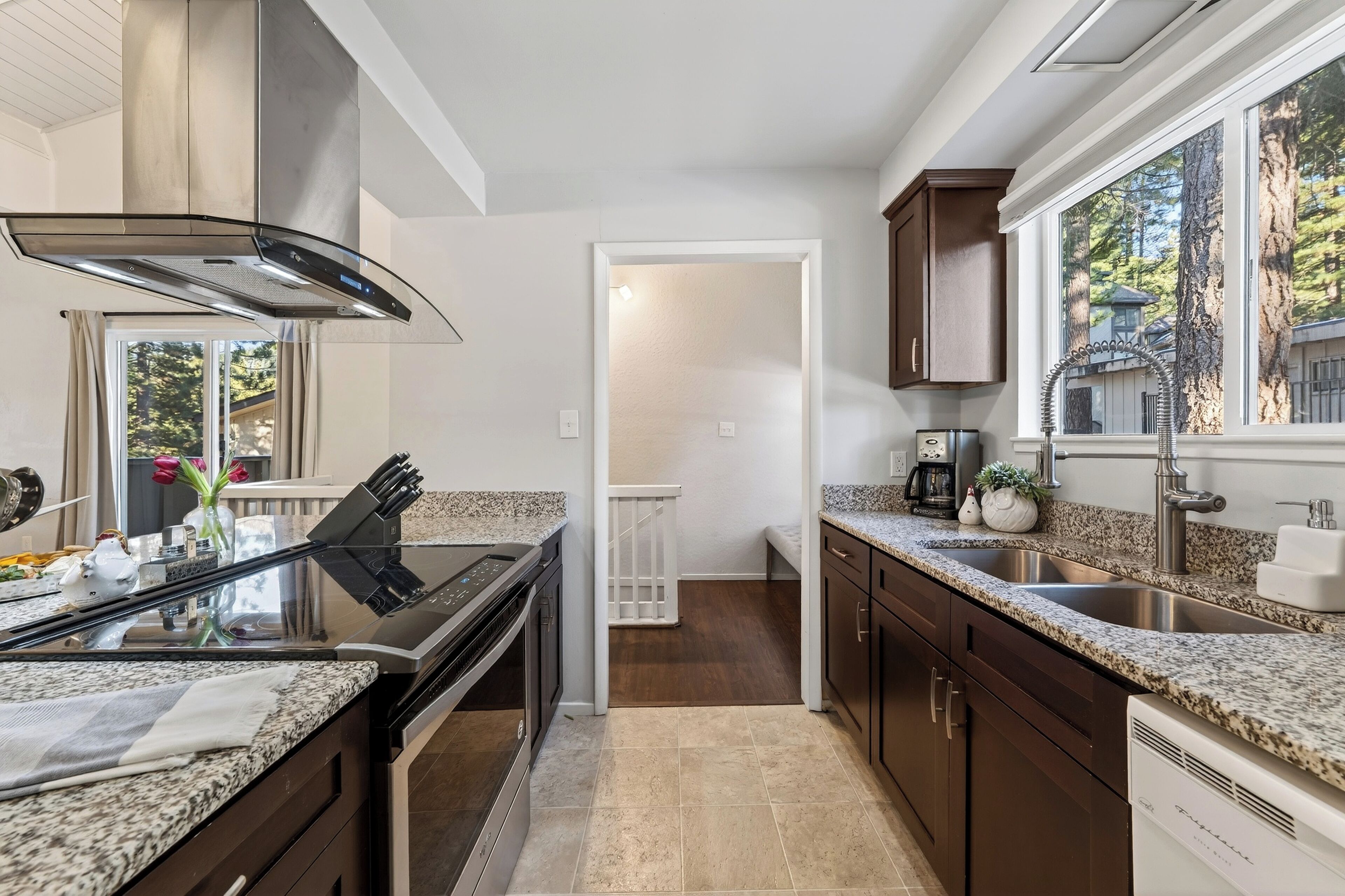 A modern kitchen with granite countertops, stainless steel appliances, and a view of the outdoors through large windows.