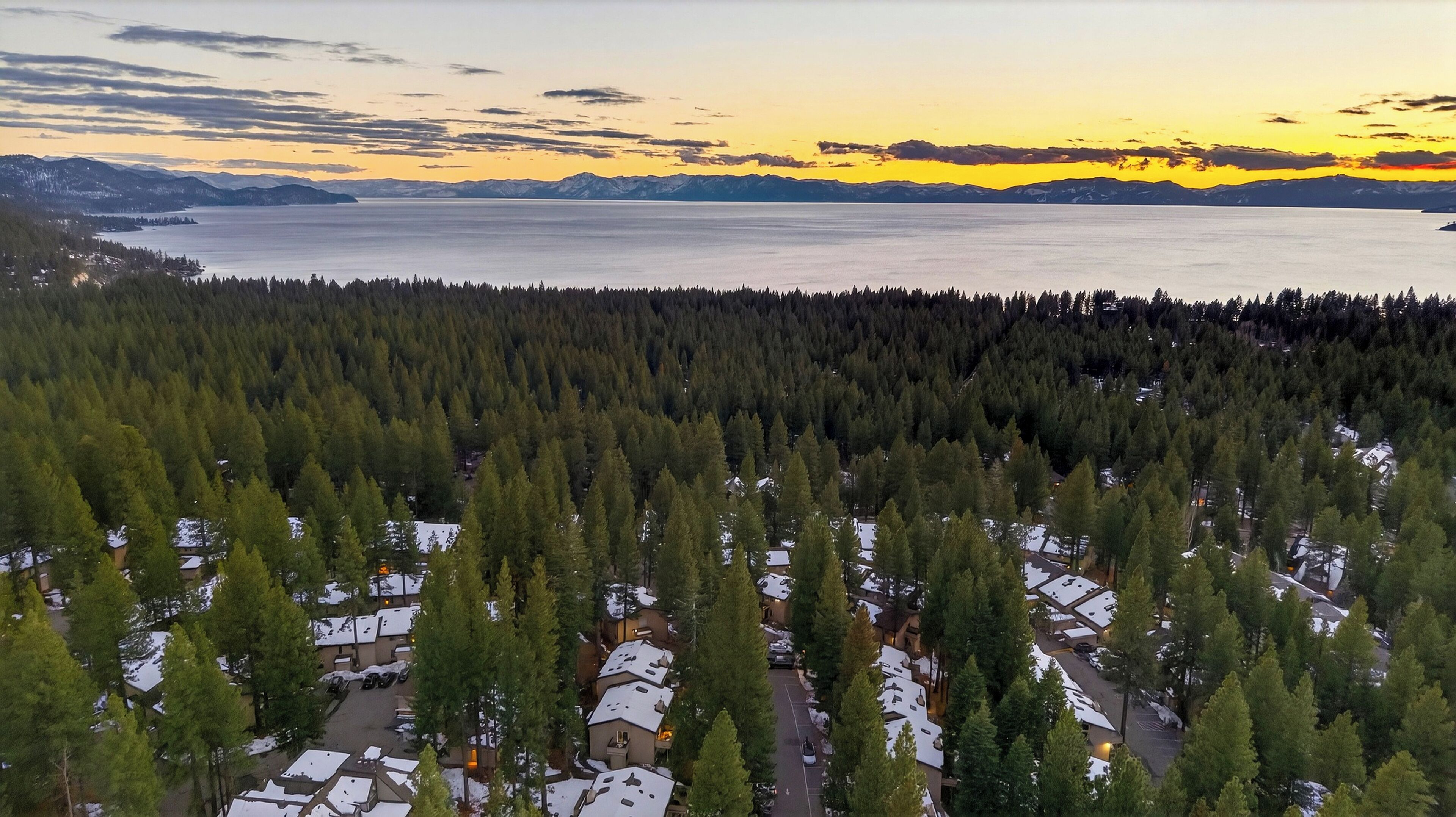Un quartier résidentiel où les maisons sont entourées d’une forêt dense, d’un plan d’eau et de montagnes lointaines.
