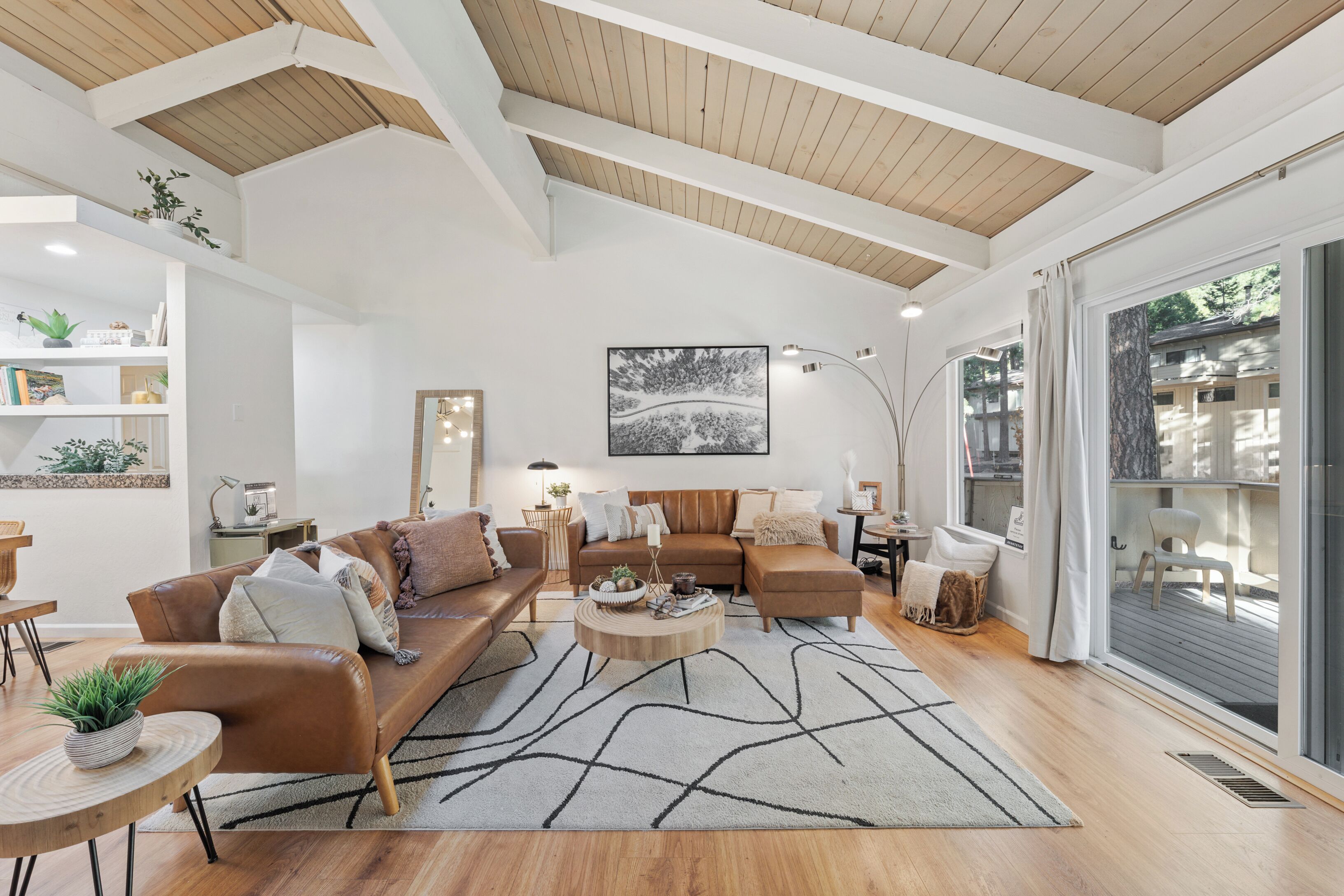 A spacious living room with a high ceiling, wooden beams, a large window with a view, and a modern fireplace.
