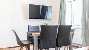 A dining area with a flat-screen TV mounted on the wall, a table with four chairs, and a window with curtains. - Modern Stay in the Heart of the City (Vienna)