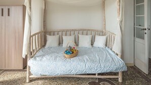 Een bed met hemel, kussens en een mand met spullen erop.