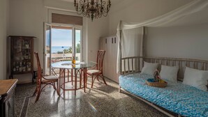 Een slaapkamer met een bed, een tafel met stoelen, een kroonluchter en uitzicht op zee.