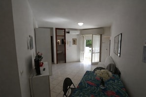 A small dining area with a table, chairs, and a vase of flowers. There is a refrigerator and a door leading to another room. - Lignano Riviera Studio With Pool Access (Lignano Sabbiadoro)