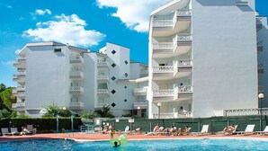Ein Schwimmbecken mit Liegestühlen und ein Gebäude mit Balkonen im Hintergrund.
