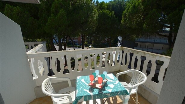 Ein Balkon mit Tisch und Stühlen, einer Brüstung und Bäumen im Hintergrund.