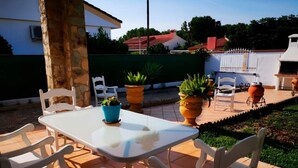 Eine Terrasse im Freien mit einem weißen Tisch und Stühlen, umgeben von Kübelpflanzen und einer Steinmauer.