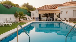 Ein Swimmingpool mit weißen Liegestühlen und einer überdachten Terrasse.