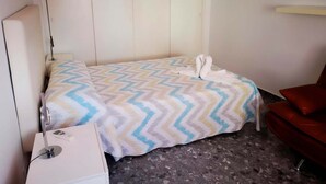 Ein kleines, ordentlich eingerichtetes Schlafzimmer mit Bett, Nachttisch und einem roten Sessel.