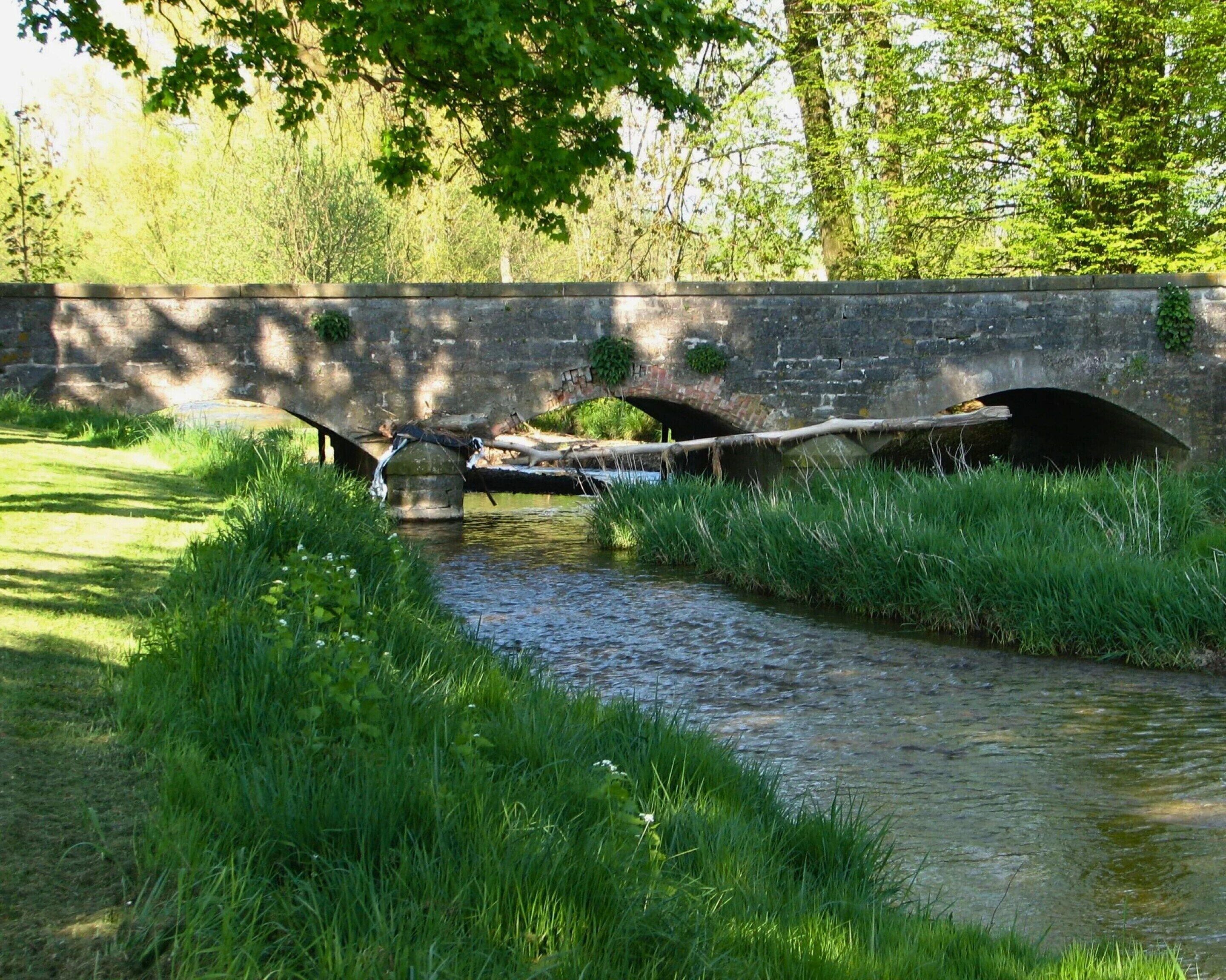 A stone bridge over a narrow stream with grass on either side.