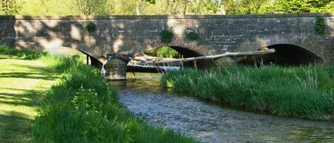 A stone bridge over a narrow stream with grass on either side.