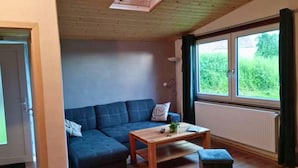 Une pièce avec un plafond en bois, un canapé bleu, une table basse en bois et une fenêtre donnant sur un paysage verdoyant.