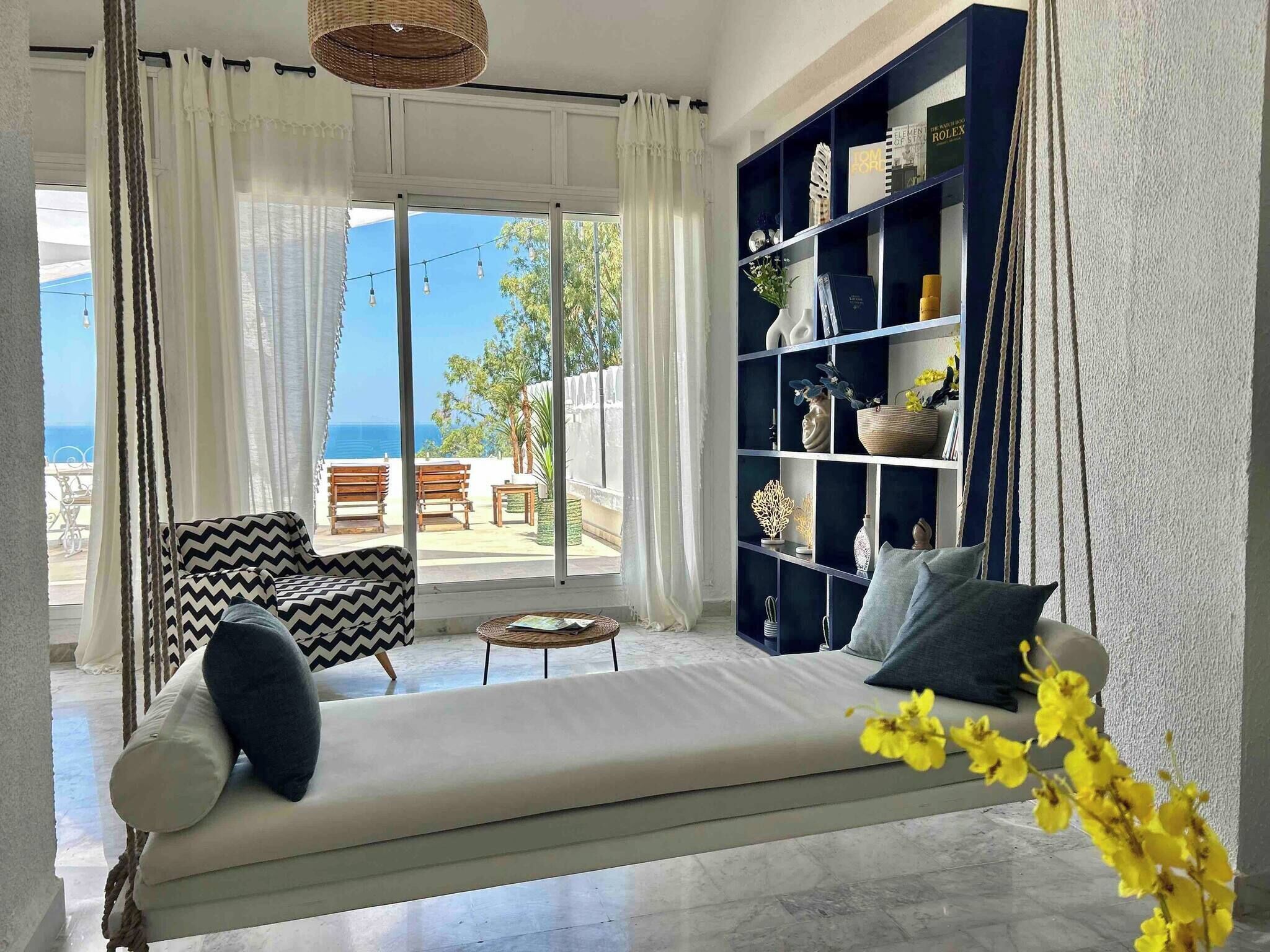 Sala de estar com sofá, estante e vista para o exterior.