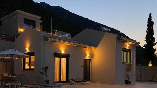 Una casa moderna con piscina, mobiliario exterior y montañas al fondo.