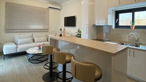 Una cocina moderna con una isla central, taburetes de bar, un televisor de pantalla plana y una zona de comedor con sofá y mesa de centro.