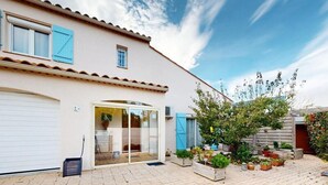 Una casa de dos pisos con garaje, puerta de cristal y jardín con plantas en macetas.