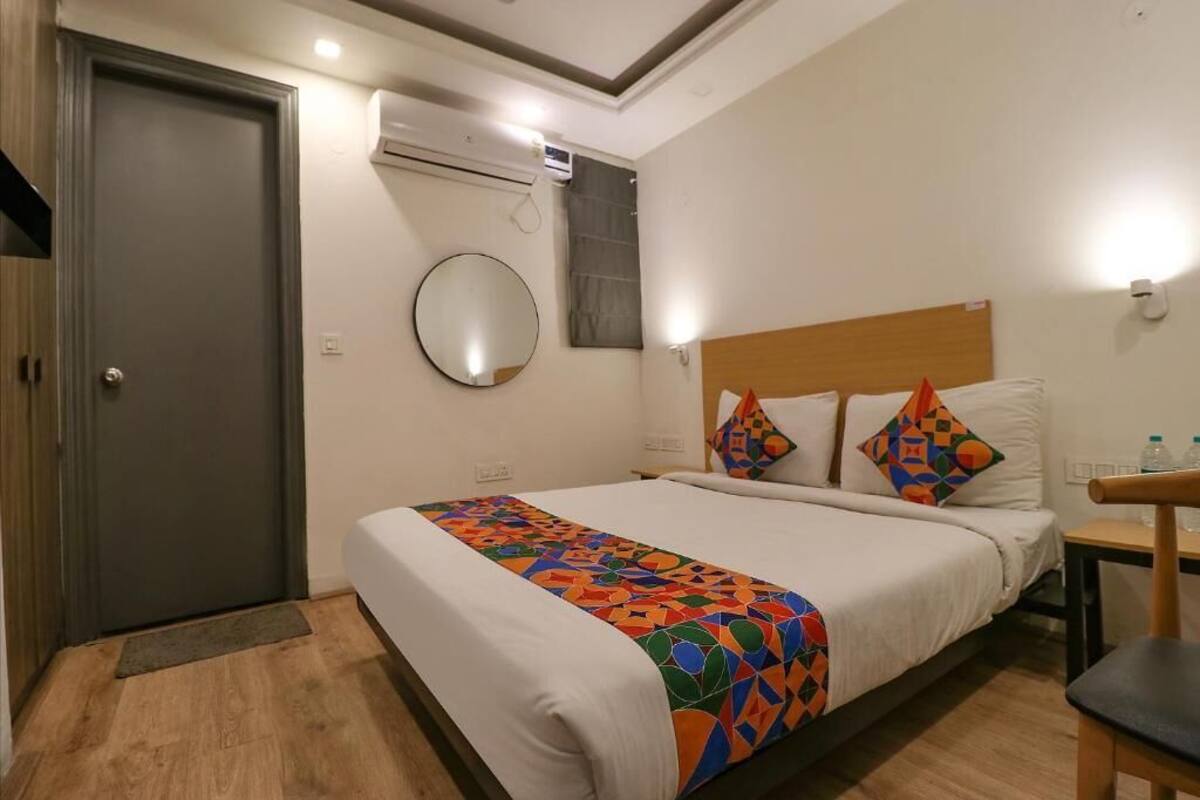 A hotel room with a bed, a bedside table, a chair, a door, and an air conditioning unit.