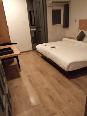 A bedroom with a bed, a wooden desk, and a small window. - Hotel The Chaitanyas Rohini (New Delhi)