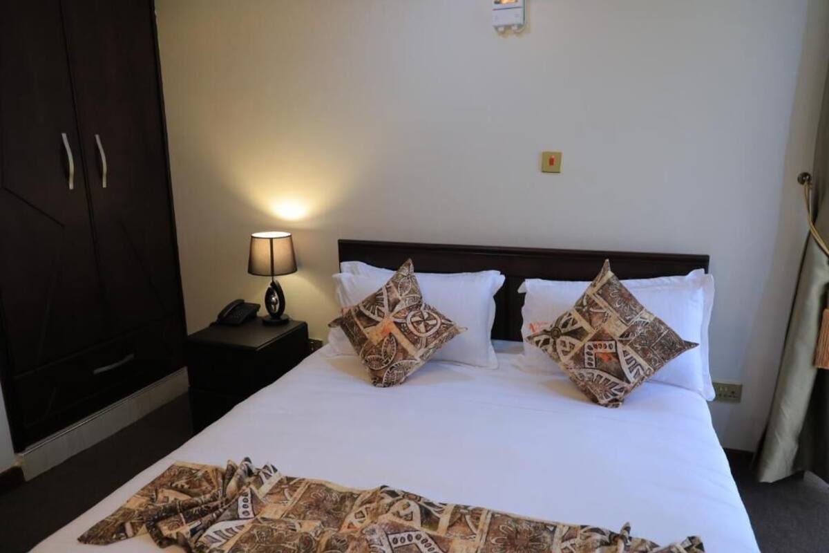 A hotel room with a large bed, two pillows, a bedside lamp, a nightstand, and a wardrobe.