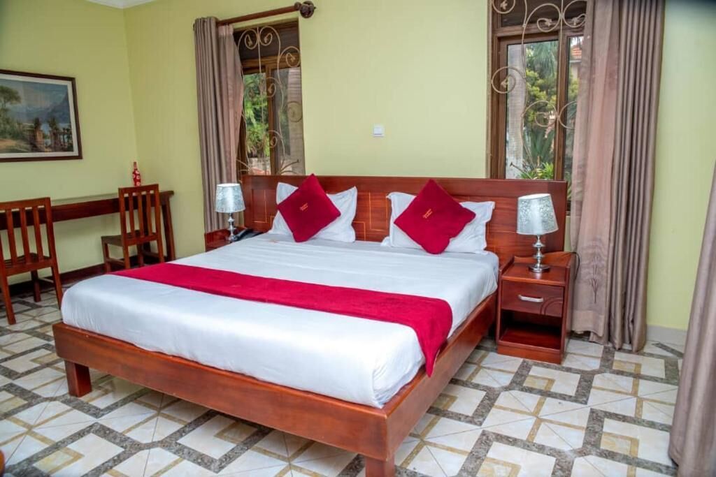 Quarto de hotel com uma cama grande, duas mesas de cabeceira, uma escrivaninha e cadeiras.