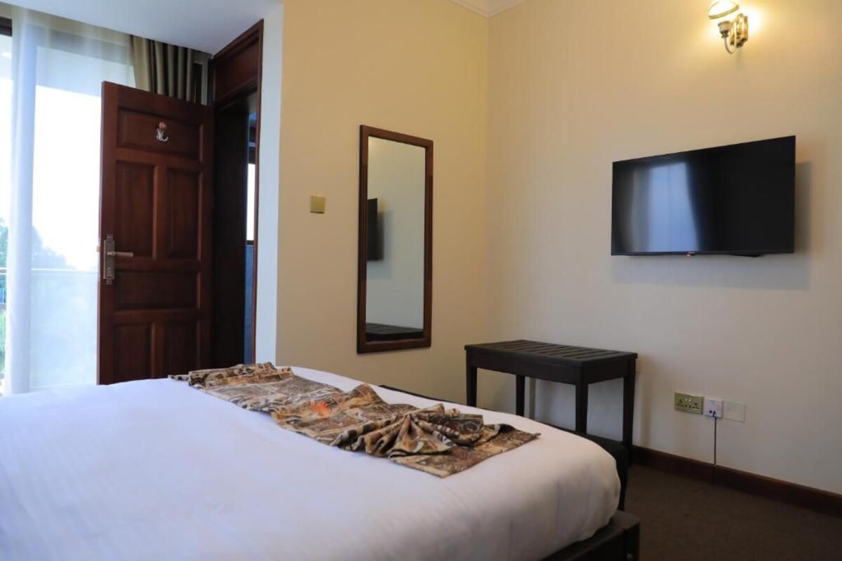 A hotel room with a bed, a TV mounted on the wall, a wooden door, and a small table.