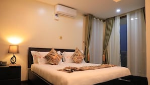 A hotel room with a bed, a nightstand, a lamp, an air conditioner, and a window with curtains. - Precious villas hotel  (Kampala)