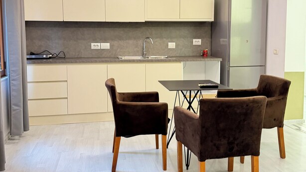 Una cocina moderna con armarios de tonos claros, un refrigerador de acero inoxidable y un comedor con dos sillas de terciopelo.