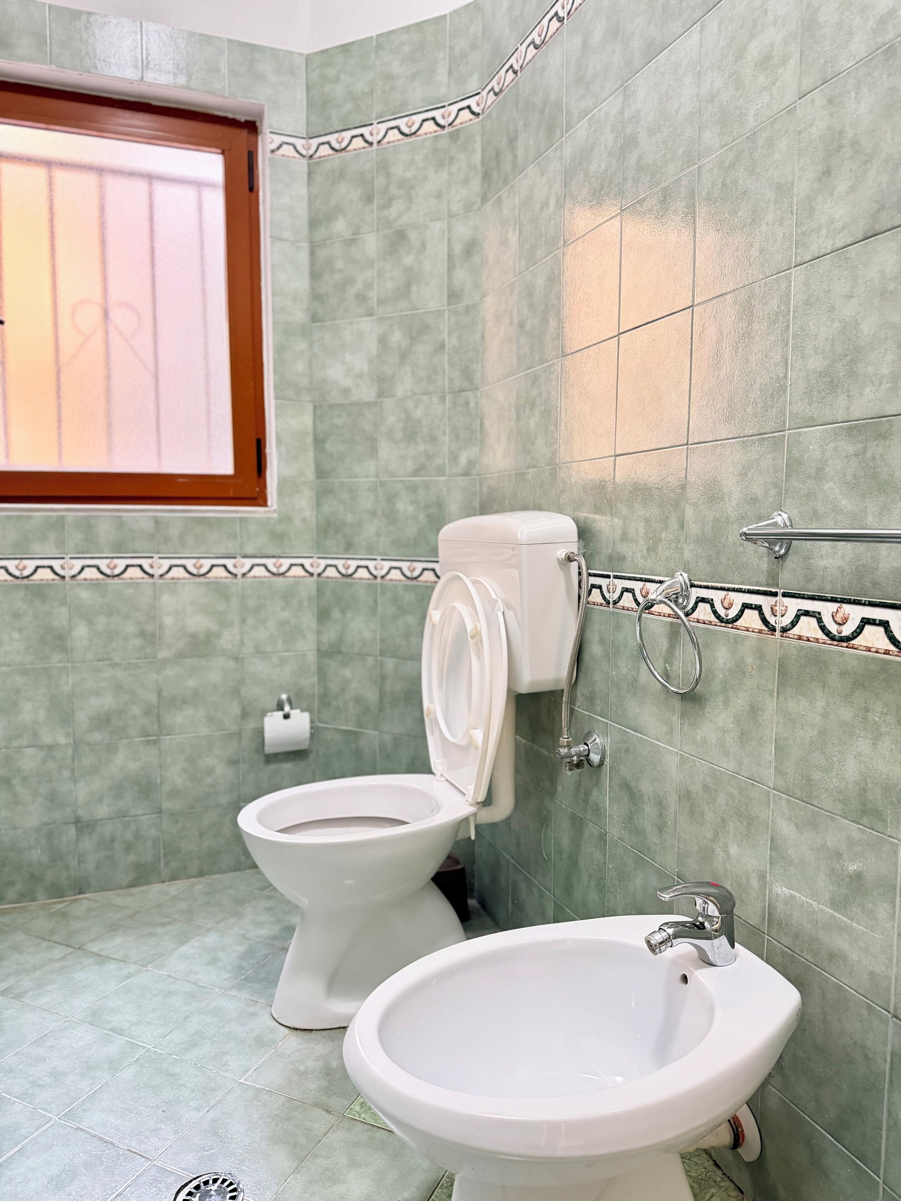A bathroom with two toilets, a bidet, and a sink.