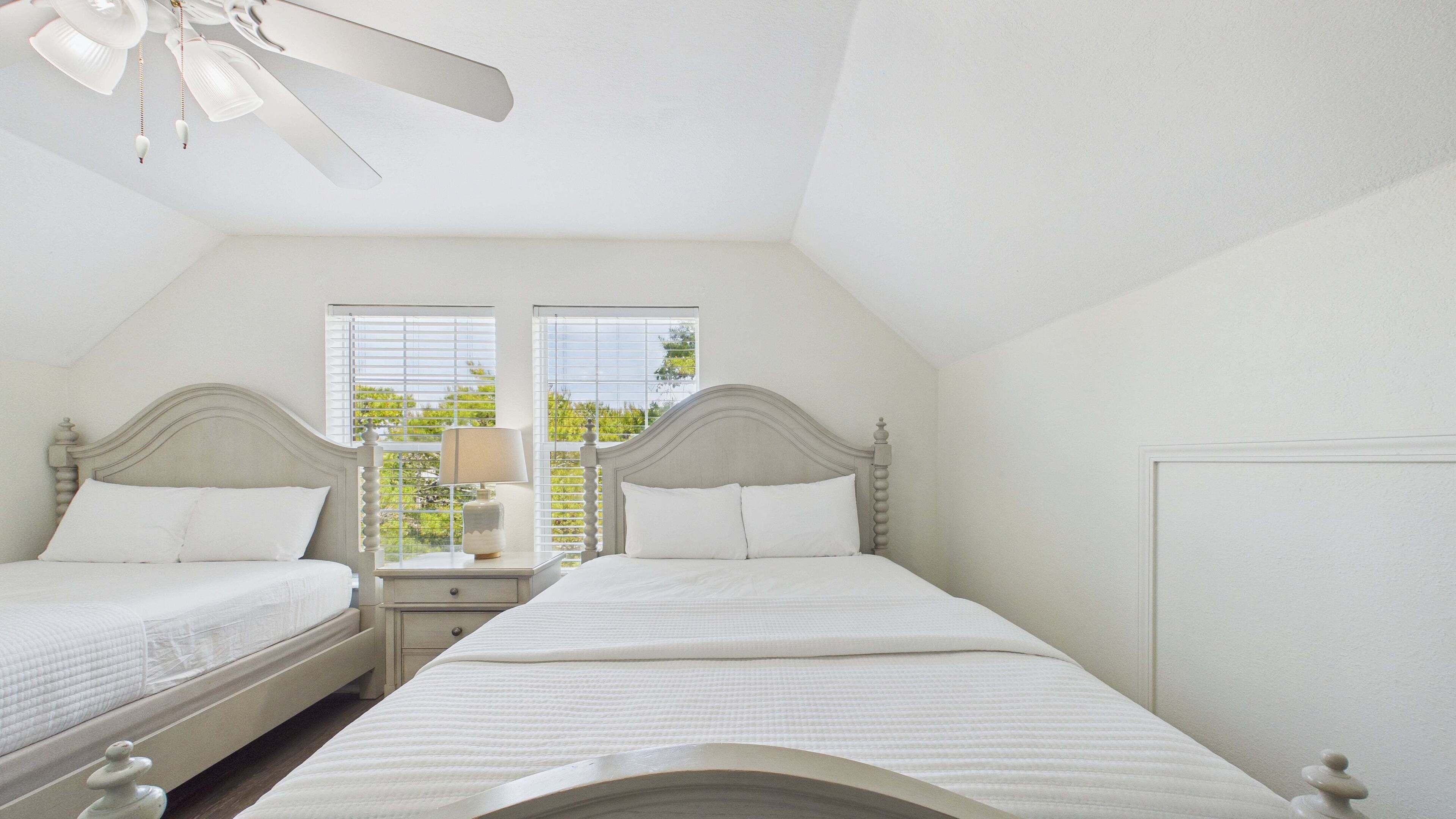 A bedroom with two beds, a nightstand with a lamp, and a ceiling fan.