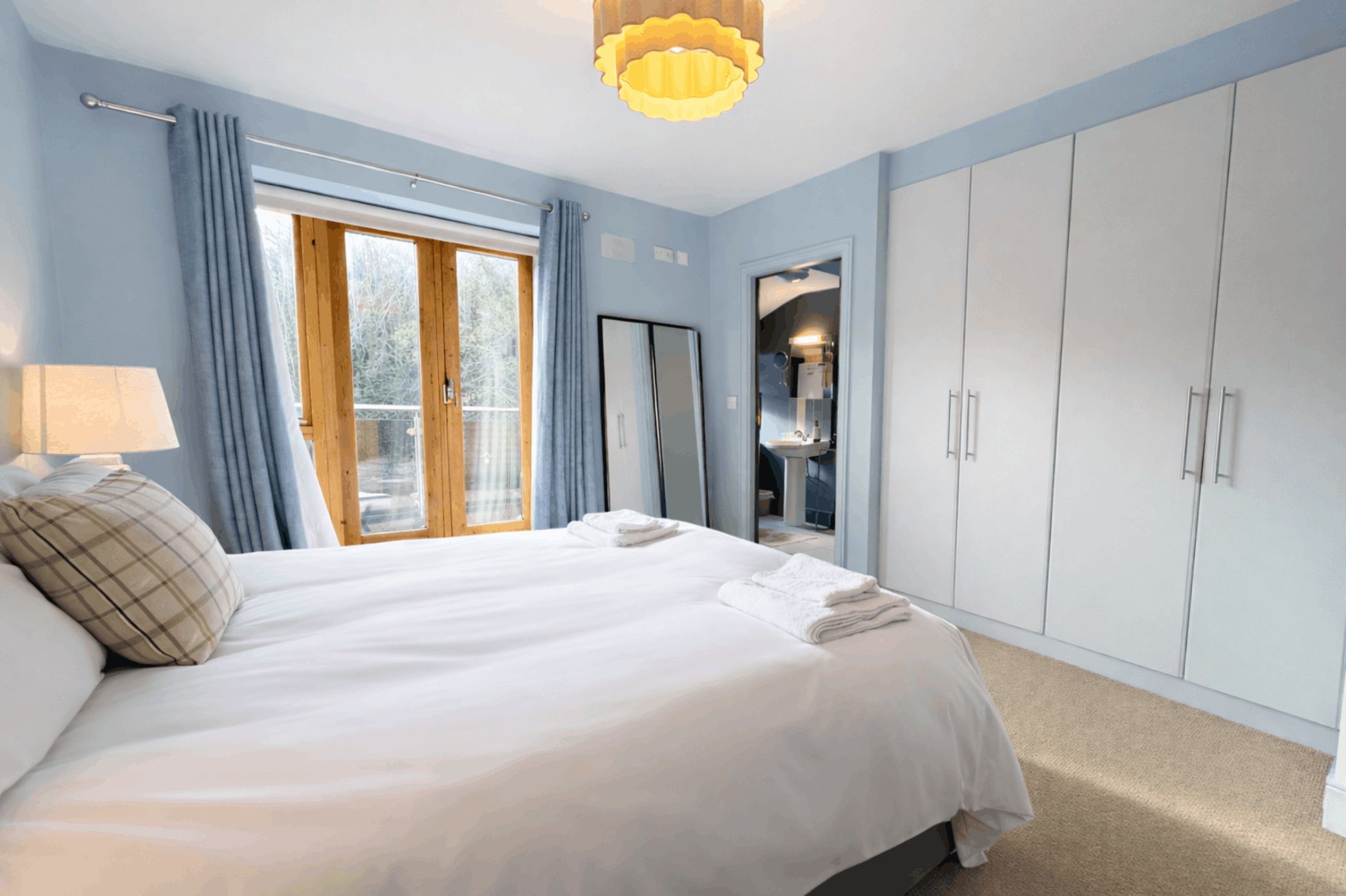 A bedroom with a large bed, a wardrobe, a mirror, and a window with curtains.