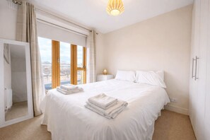 A hotel room with a large bed, a bedside table with a lamp, and a view through the window. - Bright 2BDR Split Level Apt Near Phoenix Park (Dublin)