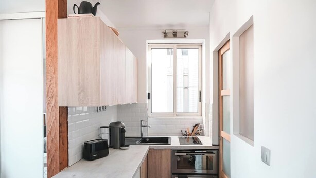 Una cocina compacta con armarios de madera, horno empotrado y ventana sobre el fregadero.