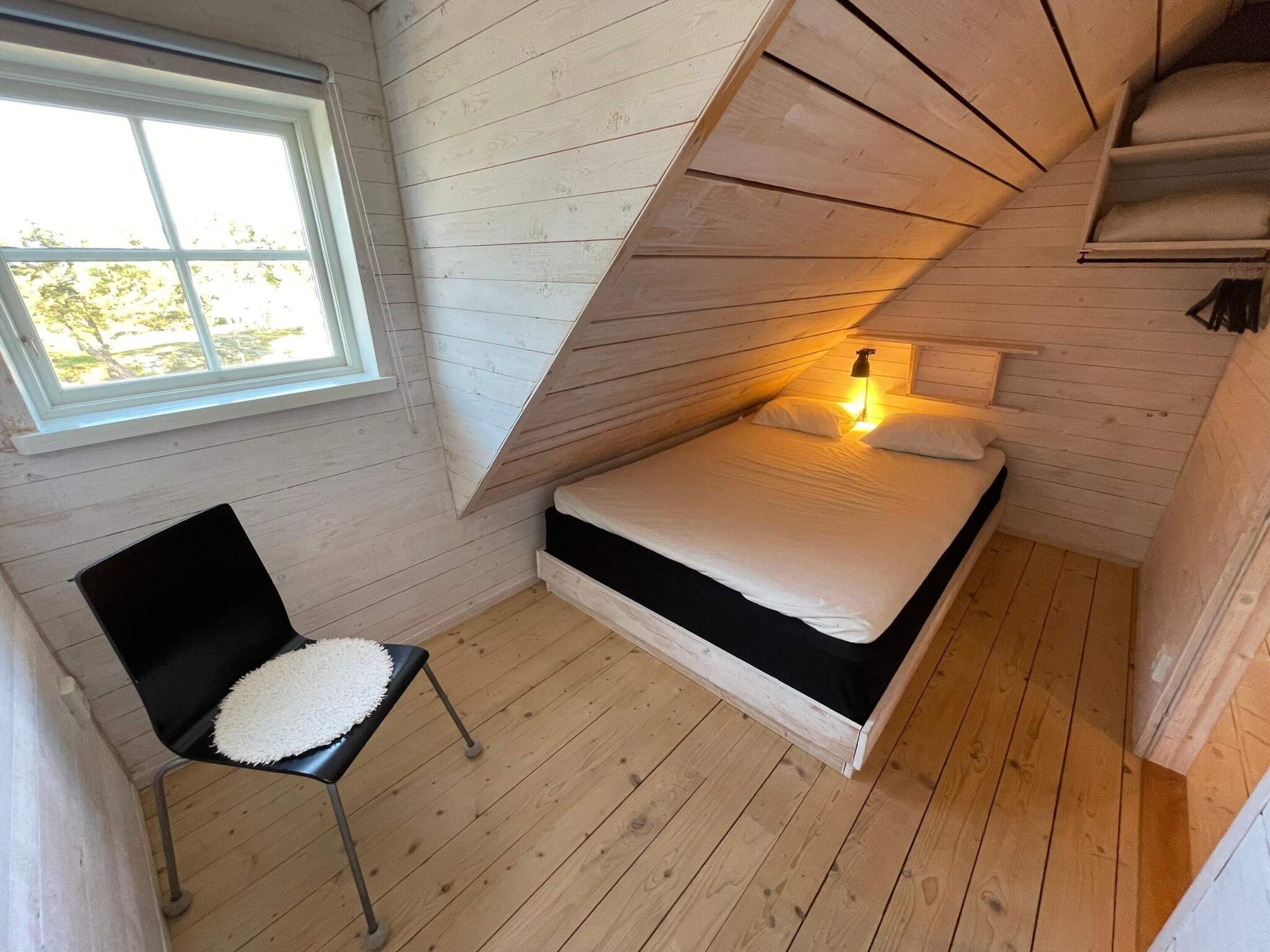 A small, sloped-roof bedroom with a single bed, a chair, and a window.