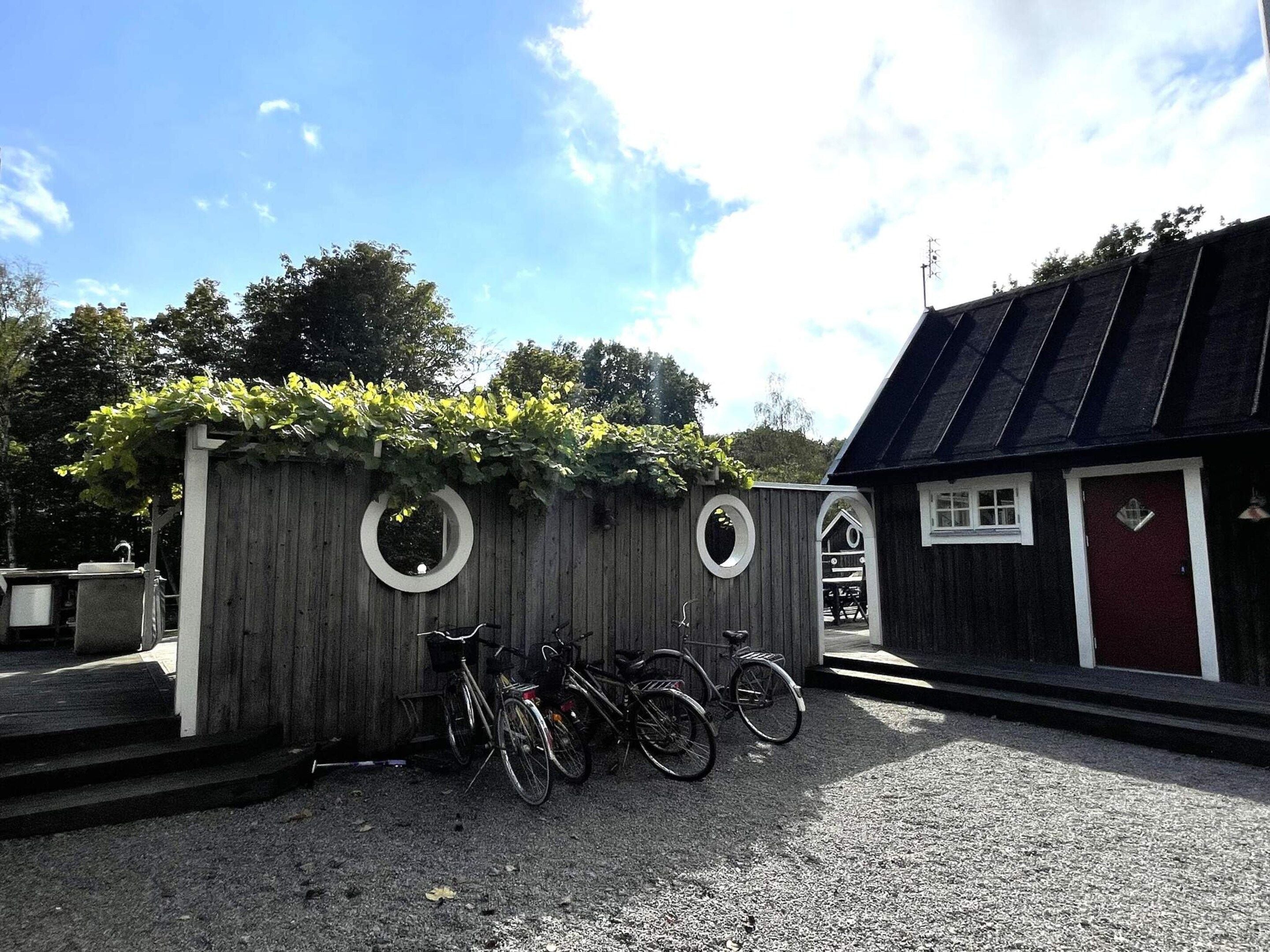 A wooden fence with circular cutouts, bicycles parked in front, and a building with a dark roof and a red door.