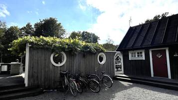 A wooden fence with circular cutouts, bicycles parked in front, and a building with a dark roof and a red door.