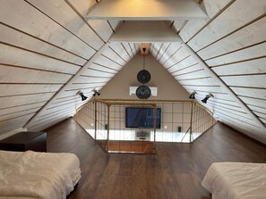 A high-ceilinged attic bedroom with a sloped ceiling, a television, and two beds. - 4 Star Holiday Home in Drottningskar (Drottningskär)