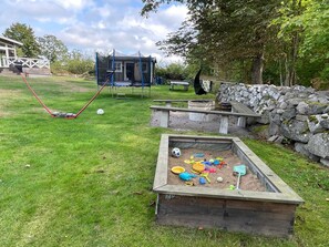 Ein Spielplatz mit Schaukeln, Sandkasten und einer kleinen Gebäude-Struktur.