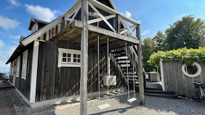 Un edificio rustico in legno, con tetto spiovente, un piccolo portico e una scala che conduce al piano superiore.