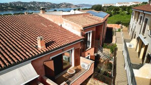 A residential building with a tiled roof, a balcony with a table and chairs, and a view of a body of water and hills in the background. - Casa di Adriana by Rentbeat (Palau)