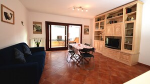 A living room with a sofa, dining table, chairs, a TV, and a bookshelf. - Casa di Adriana by Rentbeat (Palau)