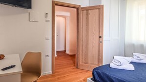 Quarto de hotel com cama, secretária e cadeira, televisão e porta que dá para outro aposento.