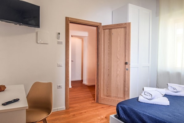 Una habitación de hotel con una cama, un escritorio con silla, un televisor y una puerta que da a otra habitación.