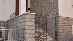 Fachada de pedra com portão de metal, porta de madeira e escadaria que leva a um andar superior.
